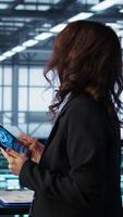 Vertical Technician in data center with tablet integrating AI driven automation tools, running predictive maintenance routines. Woman ensuring continuous uptime of server room, managing data flows, camera B video