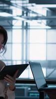 Vertical Smiling admins using laptop in data center, managing server virtualization. Cheerful IT specialist and african american man using notebook in server room, ensuring infrastructure reliability, camera A video