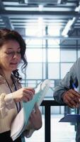 Vertical Team of IT professionals looking over data center checkup checklist paperwork. African american man and colleague collaborating in server farm reading documentation files, camera B video