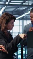Vertical Developers in data center workspace coding on laptop, analyzing metrics, optimizing storage volumes. Teamworking IT professionals in server room using notebook, ensuring seamless operations, camera B video