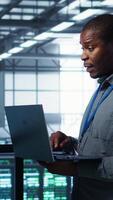 Vertical System administrators using notebook device in data center, managing server virtualization. IT specialists using laptop in server farm, sustaining long term infrastructure reliability, camera B video