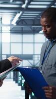 Vertical Data center team examines paperwork files in server room, reviewing system diagnostics. Server room workers looking over maintenance schedules and cybersecurity protocols, camera B video