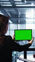 Vertical System administrators in server farm using isolated screen mockup tablet to verify settings. Data center colleagues using green screen chroma key device to monitor facility, camera B video