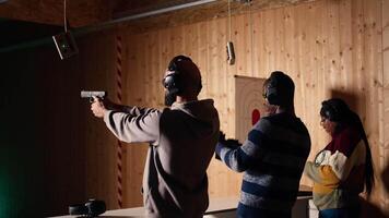 Group of friends in firing range doing recreational shooting activity with firearm, hitting bullseyes. People in shooting gallery training with handguns, sharpening skills, camera A video