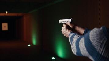 Shooting range client shoots with pistol, engaging targets at extended range. African american man at shooting ground firing lethal fire weapon, wearing protection equipment, camera A close up video