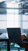 Vertical System administrators using notebook device in data center, managing server virtualization. IT specialists using laptop in server farm, sustaining long term infrastructure reliability, camera A video