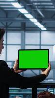 Vertical System administrators in server farm using isolated screen mockup tablet to verify settings. Data center colleagues using green screen chroma key device to monitor facility, camera A video