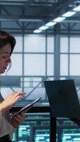 Vertical Developers in data center using laptop and tablet, executing security patches, securing firewall. Server farm workers using devices to perform vulnerability scans, ensuring data protection, camera A video