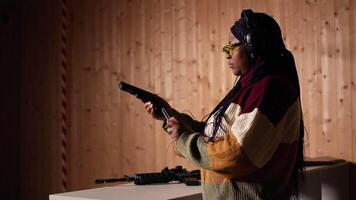 Portrait of joyous shooting range customer shooting targets with pistol, learning to operate handgun in close quarters. Smiling woman at shooting ground facility firing lethal fire weapon, camera A video