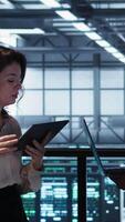 Vertical Data scientists in server room using laptop and tablet, executing security patches, verifying firewall configurations. People performing equipment vulnerability scans in data center, camera B video