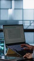 Vertical Engineer in data center operating notebook, deploying new server architectures. Server farm employee verifying settings using laptop, maintaining stable network performance, camera A video
