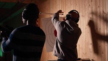 Man holds rifle, enjoying recreational shooting experience in firing range next to group of friends. People practicing with weapons in safe environment at shooting range company, camera A video