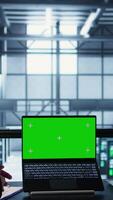 Vertical Data center system administrators using mockup laptop to review equipment diagnostics. Teamworking IT specialists adjusting server farm configurations using chroma key notebook video