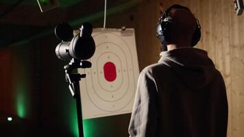 Firing range customer doing shooting activity with pistol, looking in zooming device to check if he shot bullseye. Person in shooting gallery analyzing targets shot using magnifying lens, camera A video