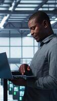 Vertical Developers in data center using laptop and tablet, executing security patches, securing firewall. Server farm workers using devices to perform vulnerability scans, ensuring data protection, camera B video