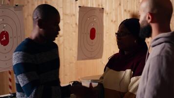 Shooting gallery worker meeting with customers, greeting them, demonstrating how to safely reload pistol. Firing range expert welcoming clients, doing hand shake, teaching weapon handling, camera B video