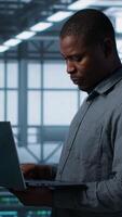 Vertical Portrait of happy system administrators in data center using devices, verifying firewall configurations. Jolly teamworking IT experts performing equipment vulnerability scans in server hub, camera A video