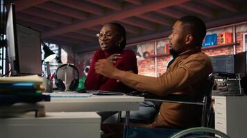 Manager coming to inclusive startup office employee in wheelchair desk to offer help. Thoughtful supervisor checking up on software development agency worker with disability, camera A video