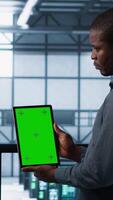 Vertical Software developers in data center using mockup tablet, observing performance analytics charts. Server hub IT professionals talking, using chroma key device, looking over graphs, camera A video