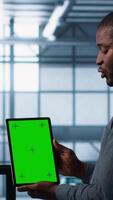Vertical Server room data scientists using mockup tablet, conducting security audits to prevent bugs. African american man with colleague in data center looking at green screen device, camera A video