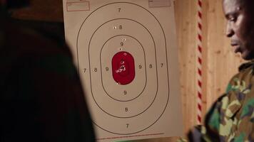 Army leader teaches recruits in shooting gallery how to shoot target center, training accuracy. Military officer instructs soldiers how to hit bullseye, explaining shooting practices, camera A closeup video