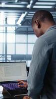 Vertical Engineer in data center with laptop automating routine maintenance tasks, executing diagnostic scripts. Man coding on notebook, adjusting power settings, validating server configurations, camera B video