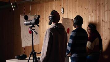 Friends in firing range doing recreational shooting, using magnifying lens to see targets. People training with handguns, sharpening skills, zooming to check points scored on bullseyes, camera A video