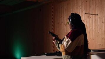 Person wearing safety equipment loading bullets cartridge in pistol during firearm practice session at shooting range. Woman reloading gun, pointing weapon at targets, learning self defense, camera A video