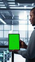 Vertical Server room data scientists using mockup tablet, conducting security audits to prevent bugs. African american man with colleague in data center looking at green screen device, camera B video