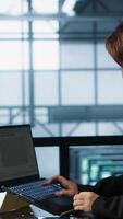 Vertical Admin in data center using laptop to update storage arrays, configuring network virtualization. Woman in server room holding coffee cup, verifying settings to maintain stable performance, camera A video