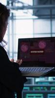 Vertical Cybersecurity expert in data center frantically trying to counter a hacker attack. Server room worker under pressure to secure sensitive information after threat alert received on laptop, camera A video