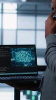 Vertical Software developers using AI tech on laptop in data center managing server virtualization. IT expert coding on notebook in server room using artificial intelligence, finetuning network, camera A video