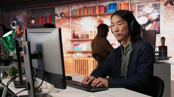 Senior admin coding advanced AI algorithm in startup office, refining machine learning models to enhance automation, wearing headphones. CTO manager listening music and coding, camera A video