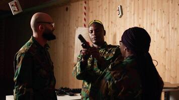 Army commander talking with recruits in shooting gallery, showing them how to reload firearms. Military officer instructing soldiers on how to load ammunition into pistol, camera A video