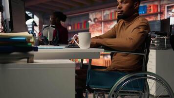 Man in wheelchair working in inclusive AI tech agency providing software development services. IT worker with disability using machine learning to streamline coding process in startup office, camera A video