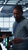 Vertical Computer scientists in data center using tablet to develop disaster recovery plans. IT professionals in server farm discussing, testing failover scenarios, protecting data during disruptions, camera B video