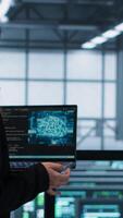 Vertical AI technology used by data center software developers reviewing equipment diagnostics. Programmers coding on laptop using artificial intelligence, adjusting server farm configurations, camera A video