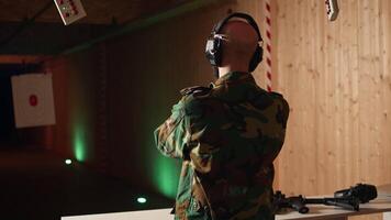 Army soldier in shooting range reloads pistol, shooting target, testing accuracy, looking at results. Military man in firing range practices with weapon, checking to see if he shot bullseye, camera A video