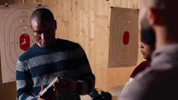 Shooting range safety officer demonstrating how to safely reload firearms to customers, ensuring they follow rules. Firing range employee teaching proper weapon handling and usage, camera B video