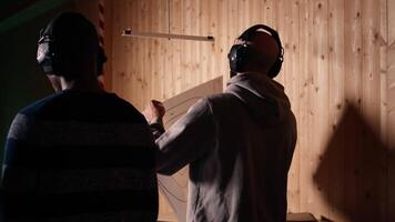 Man in firing range doing shooting sport, looking at results on paper target. Person wearing safety gear training with handgun, sharpening skills, checking points scored on bullseye, camera A video