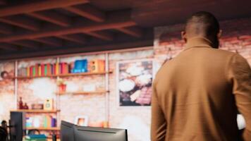 Company personnel sitting at desks in startup office, imputing data on computers. Man entering venture agency room holding laptop next to staff members in solving tasks during job shift, camera A video