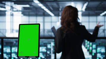 Close up of mockup tablet and data center engineers developing disaster recovery plans. Focus on isolated screen device in front of server farm colleagues testing failover scenarios, camera B video