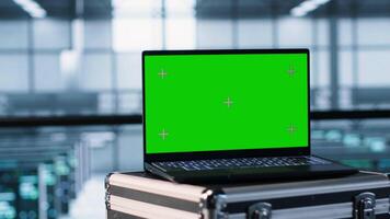 Green screen laptop in front of data center engineers in blurry background calibrating energy usage, inspecting servers configuration, supporting sustainable infrastructure, camera A video