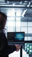 Vertical AI technology used by data center software developers reviewing equipment diagnostics. Programmers coding on laptop using artificial intelligence, adjusting server farm configurations, camera B video