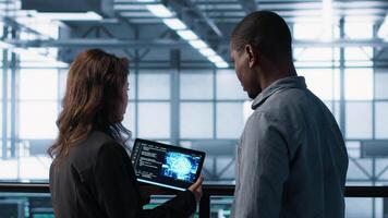 Data center technicians deploying AI driven management tools using tablet. Server farm coworkers inspecting server clusters, updating network topologies using artificial intelligence, camera A video