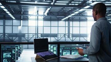 Technician in data center with laptop and tablet integrating AI driven automation tools. Server room worker using artificial intelligence on devices, ensuring continuous uptime, camera B video