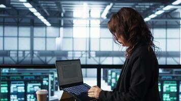 Technician using laptop in data center, finetuning network protocols, holding coffee cup. Woman in server room coding on notebook, enforcing advanced security measures, camera B video