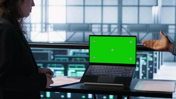 Coworkers in data center using mockup laptop, integrating green technologies. IT experts in server room using chroma key notebook to implement sustainable energy solutions, camera A close up video