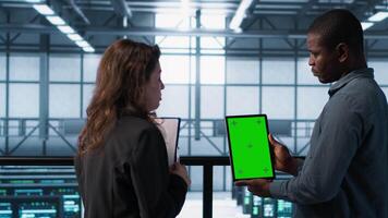 Software developers in data center using mockup tablet, observing performance analytics charts. Server hub IT professionals talking, using chroma key device, looking over graphs, camera A video