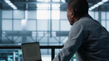Technician in data center using laptop, adjusting power management settings, using programming languages. Man in server room optimizes resource utilization, maintaining stable infrastructure, camera A video